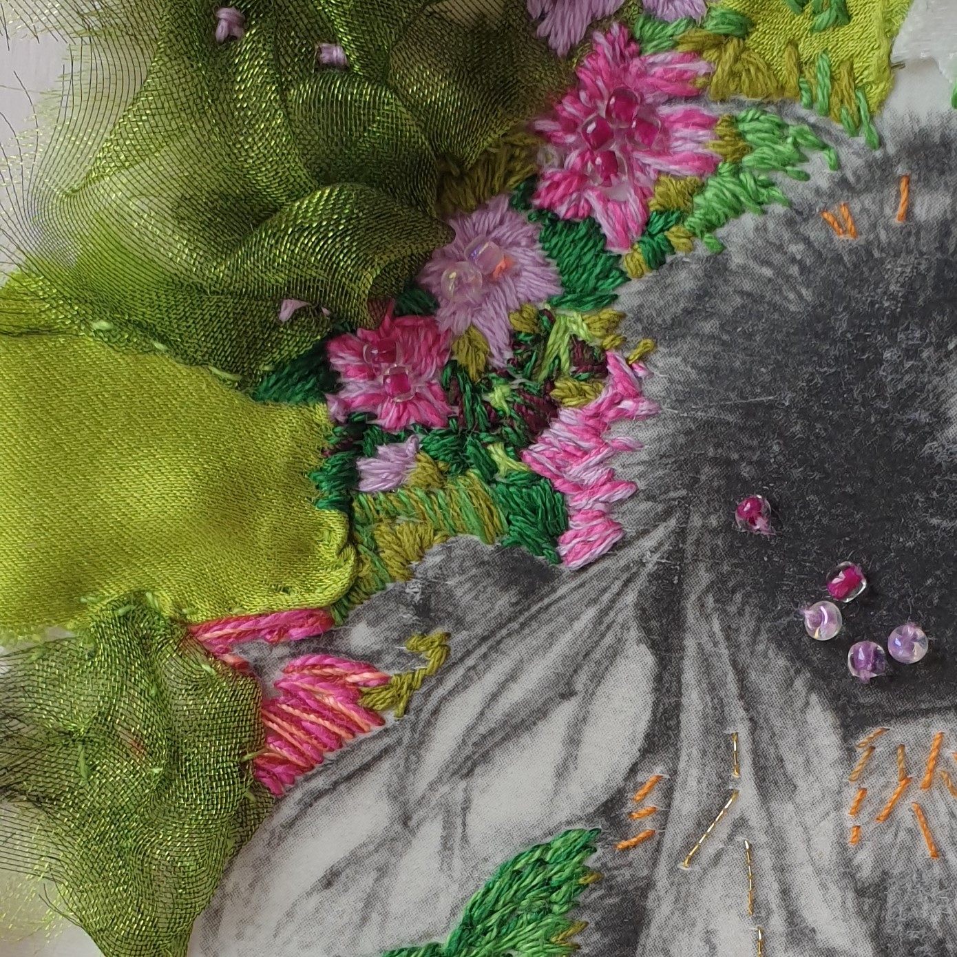 Close up of hand embroidered colourful flowers around monochrome image transfer drawing of bumblebee on white satin