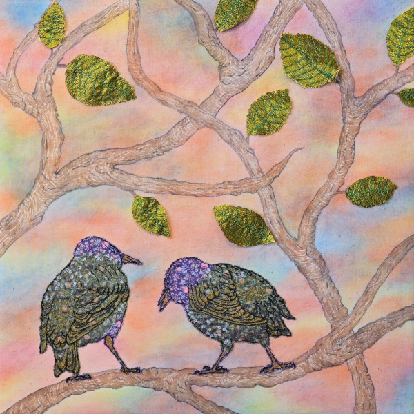 Camden Starlings by Fiona Scutcher textile art of two shimmery embroidered starlings sitting next to each other on a leafy branch with a sunset sky in the background in oranges and pinks