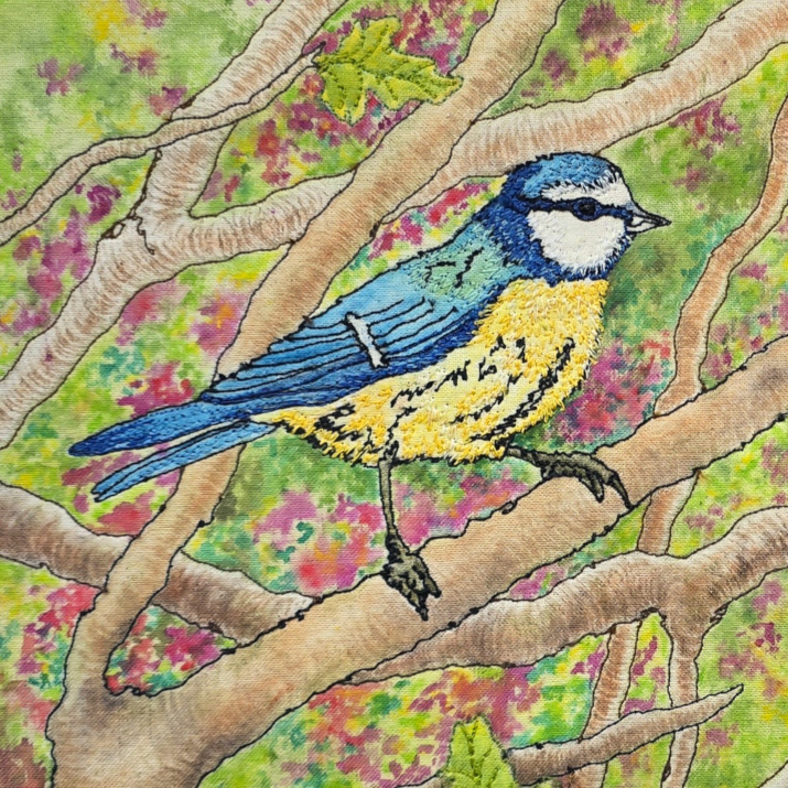 colourful embroidered bluetit textile art with painted and stitched background of branches leaves and berries